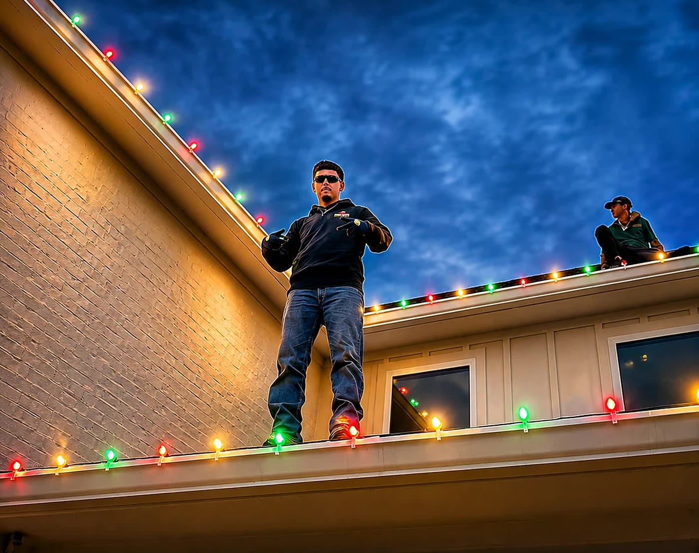 TruLights crew standing on a finished roofline at dusk with colored holiday lights running the full eave